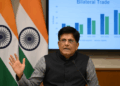 Piyush Goyal habla ante la prensa con banderas de India y EE. UU. y un gráfico comercial detrás.