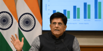 Piyush Goyal habla ante la prensa con banderas de India y EE. UU. y un gráfico comercial detrás.