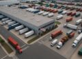 Vista aérea de centro logístico industrial con camiones y contenedores en movimiento.