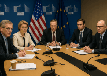 Funcionarios con gesto serio en sala de la Comisión Europea, con banderas de EE.UU. y la UE al fondo.