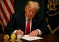 Donald Trump firma la Genius Act con criptomonedas físicas distribuidas sobre el escritorio presidencial.