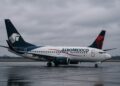 Aviones de Aeroméxico y Delta en una pista mojada bajo cielo nublado, con ambiente frío y corporativo.