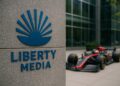 Fachada de Liberty Media con logotipo visible y auto de Fórmula 1 desenfocado al fondo.