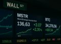 Pantallas bursátiles en Wall Street mostrando en paralelo las cotizaciones de MSTR y Bitcoin en verde.