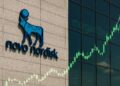 Fachada de la sede de Novo Nordisk con su logotipo visible y gráficos financieros ascendentes proyectados.