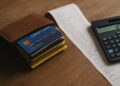 Billetera llena de deudas de tarjetas junto a una factura extensa y una calculadora encendida sobre mesa de madera