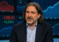 David Zervos de cabello largo en entrevista televisiva, con gráficos financieros en pantallas de fondo
