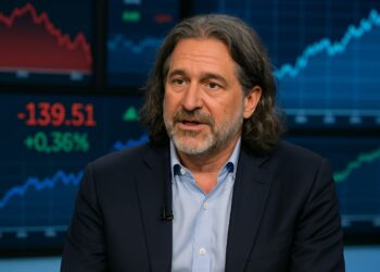 David Zervos de cabello largo en entrevista televisiva, con gráficos financieros en pantallas de fondo