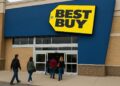 Fachada de tienda Best Buy con clientes entrando por la puerta principal y logo amarillo visible