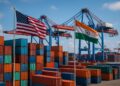 Contenedores apilados en puerto con grúas y banderas de Estados Unidos e India ondeando en contraste con aranceles