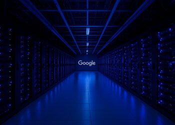 Pasillo de servidores en sala iluminada en azul con logo de Google al fondo representando centro de datos