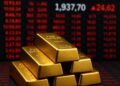 Lingotes de oro apilados frente a pantallas rojas de mercado con precios en aumento.