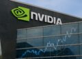 Fachada de sede Nvidia con logo verde y reflejo de gráficos bursátiles en vidrio