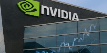 Fachada de sede Nvidia con logo verde y reflejo de gráficos bursátiles en vidrio