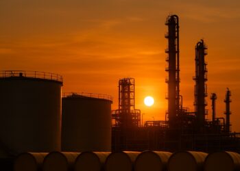 Refinería industrial al atardecer con tanques de almacenamiento de petróleo y torres en silueta
