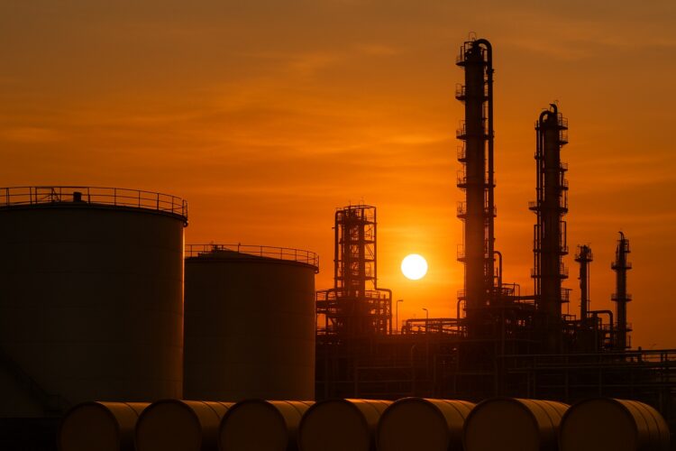 Refinería industrial al atardecer con tanques de almacenamiento de petróleo y torres en silueta