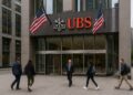 Fachada de la sede de UBS en distrito financiero con peatones y banderas de Estados Unidos ondeando