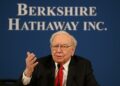 Warren Buffett hablando en reunión anual con fondo de logo de Berkshire Hathaway