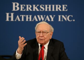 Warren Buffett hablando en reunión anual con fondo de logo de Berkshire Hathaway