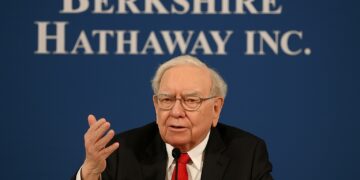 Warren Buffett hablando en reunión anual con fondo de logo de Berkshire Hathaway