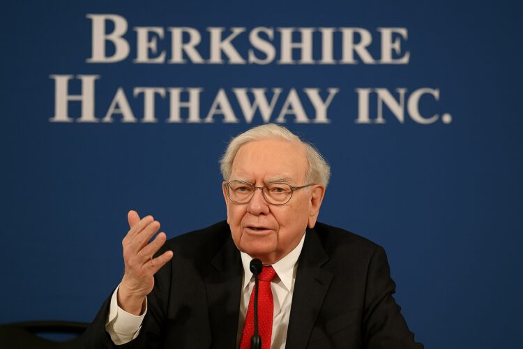 Warren Buffett hablando en reunión anual con fondo de logo de Berkshire Hathaway