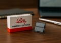 Acciones de Eli Lilly y Broadcom representadas con caja farmacéutica y chip en un escritorio editorial.