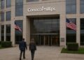 Fachada de ConocoPhillips con dos empleados entrando al edificio y banderas ondeando