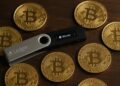  Un hardware wallet Ledger sobre mesa de madera rodeado de monedas físicas de Bitcoin