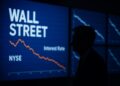 Silueta de Jerome Powell frente a pantallas de Wall Street con gráficos de tasas en descenso