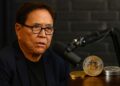 Robert Kiyosaki en un pódcast con micrófonos y monedas de Bitcoin, oro y plata en la mesa.