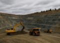 Excavadora y camiones trabajando en mina de oro a cielo abierto en Canadá con terrazas de roca