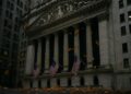 Fachada de la Bolsa de Nueva York con banderas y hojas otoñales cayendo en una atmósfera sobria de septiembre.