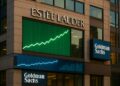 Fachada de la sede de Estée Lauder al atardecer con pantallas que muestran gráficos de crecimiento y el logotipo de Goldman Sachs.