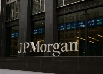 Edificio de JPMorgan en Nueva York con logo visible y pantallas de cotizaciones bursátiles al fondo