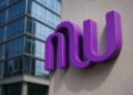 Logo de Nu Holdings en gran formato con textura metálica y luz natural sobre fondo neutro.