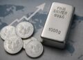 Lingotes y monedas de plata sobre mapa financiero, reflejando el alza de la plata cerca de 50 USD.