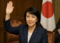 Sanae Takaichi levanta la mano en el parlamento japonés con fondo institucional y bandera nacional