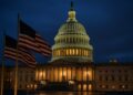 Vista nocturna del Capitolio estadounidense con luces encendidas terminando el cierre de gobierno y banderas ondeando en primer plano