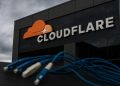 Logo de Cloudflare en edificio corporativo con cables de fibra desconectados en primer plano.