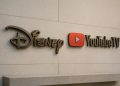 Logos metálicos de Disney y YouTube TV integrados en una pared elegante tras cerrar un acuerdo.