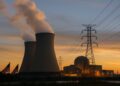 Torres de enfriamiento con vapor y líneas eléctricas frente a planta nuclear al atardecer