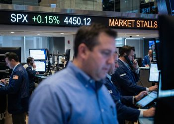 Interior de un piso de remates activo; una pantalla LED al fondo muestra "SPX +0.15%" y "MARKET STALLS" entre operadores de Bank of america trabajando.