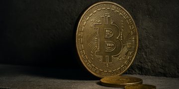 Moneda física de Bitcoin apoyada contra una superficie rugosa, evocando presión y pérdidas.