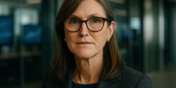 Cathie Wood en primer plano con fondo financiero moderno alusivo a inversión en criptomonedas.