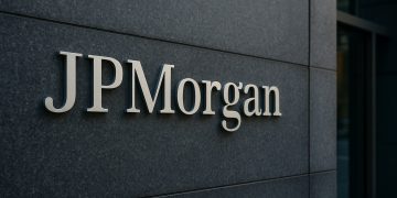 Logo de JPMorgan en gran placa metálica sobre muro oscuro, protagonista de la escena.