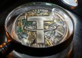 Una lupa revela el interior de una moneda física de Tether, mostrando una mezcla de circuitos, oro y dólares triturados.