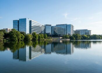 Vista panorámica exterior de la sede corporativa de Oracle en Austin, Texas, ubicada frente al lago Lady Bird. La imagen muestra la arquitectura moderna de vidrio del edificio reflejada en el agua bajo una luz diurna brillante, rodeada de vegetación, proyectando una imagen de innovación tecnológica y solidez empresarial.