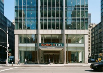 Fotografía urbana que muestra la vista frontal a nivel de calle de la entrada del moderno edificio de oficinas ubicado en 605 3rd Avenue, Nueva York. Un letrero prominente sobre las puertas de vidrio indica "GLOBAL X ETFs". Peatones caminan por la acera y vehículos circulan por la calle bajo la luz del día.