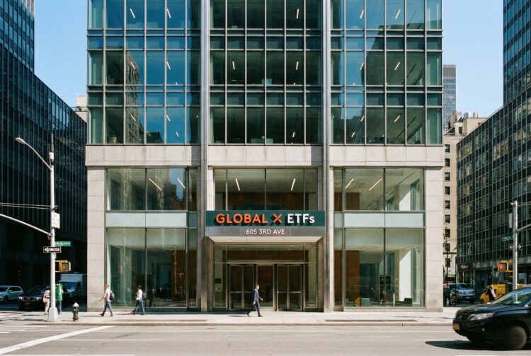 Fotografía urbana que muestra la vista frontal a nivel de calle de la entrada del moderno edificio de oficinas ubicado en 605 3rd Avenue, Nueva York. Un letrero prominente sobre las puertas de vidrio indica "GLOBAL X ETFs". Peatones caminan por la acera y vehículos circulan por la calle bajo la luz del día.