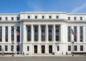 Vista frontal y simétrica de la fachada estilo Beaux-Arts del edificio de la Reserva Federal en Washington D.C. La imagen destaca la solidez del mármol blanco y las columnas clásicas bajo luz natural, simbolizando la autoridad central del banco central de EE.UU.